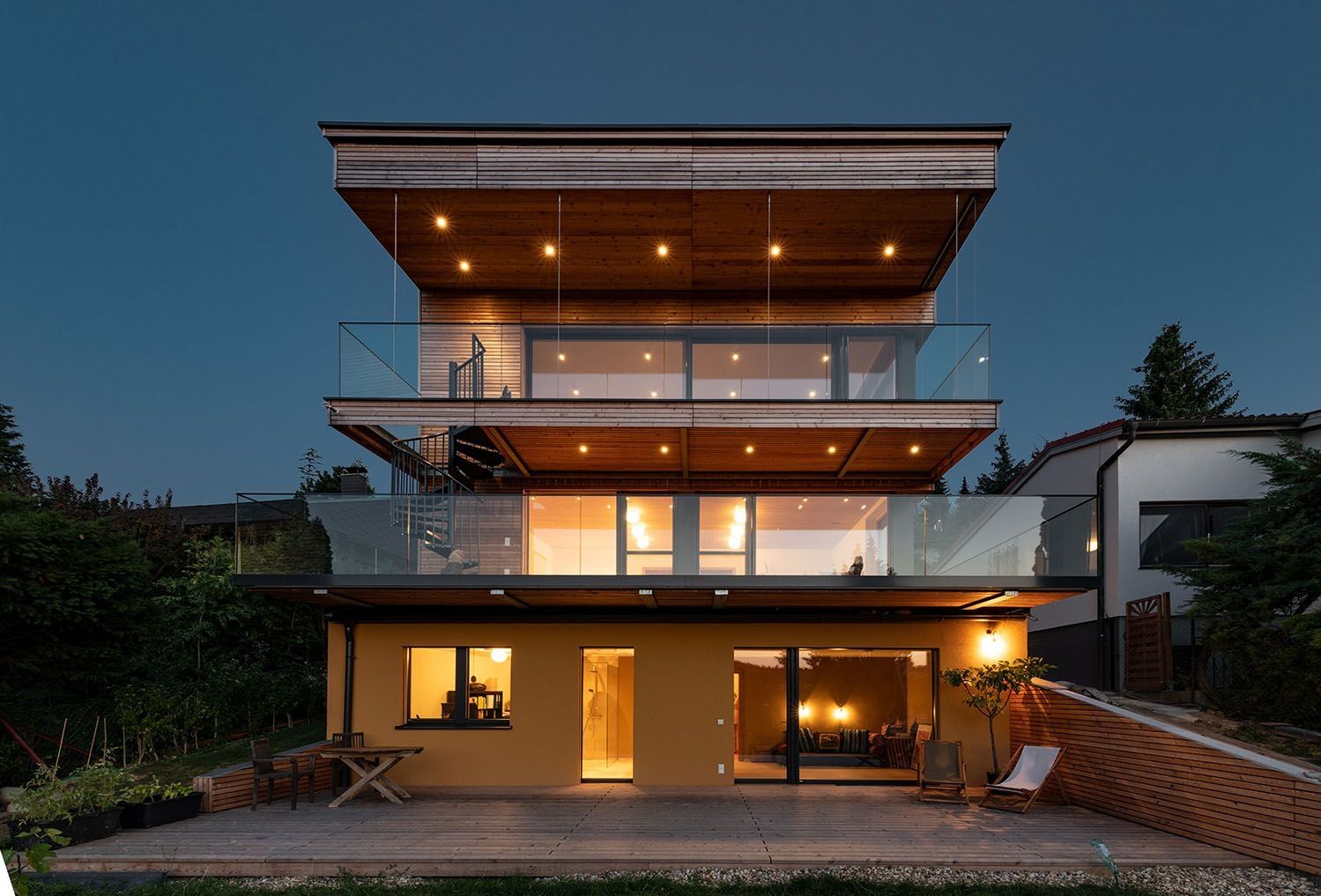 Modernes Mehrfamilienhaus mit Glasbalkonen und Holzfassade bei Abenddämmerung