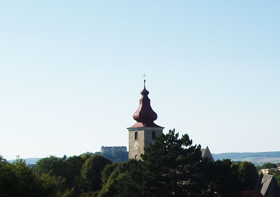 Kirchturm ragt über Bäume in hügeliger Landschaft